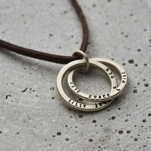 Op de afbeelding: Een zilveren ketting met een dubbele ring hanger. De ringen zijn gegraveerd met de namen "Kate", "Lilly", "Grace", "Jan", "Ben" en "Will".