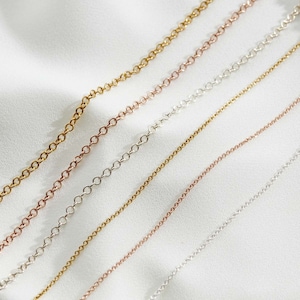 May include: A set of five delicate chain necklaces in different lengths and colors, including gold, silver, and rose gold. The chains are arranged in a diagonal pattern on a white background.