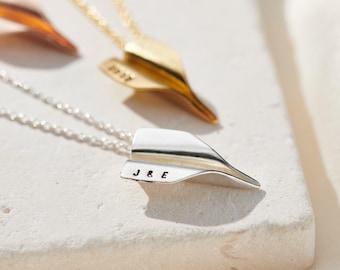 May include: Two silver necklaces with paper airplane pendants. The pendant on the bottom necklace has the initials "J&E" engraved on it.