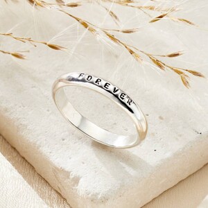 May include: A silver ring with the word "FOREVER" engraved on the band.