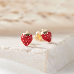 May include: A pair of gold-toned stud earrings featuring a red enamel strawberry design.