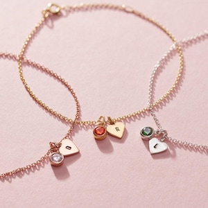 May include: Three gold chain bracelets with heart charms and small gemstones. The charms are engraved with the letters "D", "R", and "L".