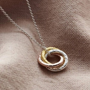 May include: A silver chain necklace with a pendant made of three interlocking rings. The rings are made of silver, rose gold, and gold.