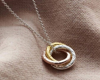 May include: A silver chain necklace with a pendant made of three interlocking rings. The rings are made of silver, rose gold, and gold.