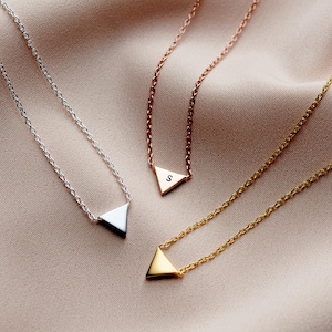 Puede incluir: Tres delicados collares con colgantes triangulares. Los colgantes están hechos de plata, oro y oro rosa y cada uno tiene una letra 'S' grabada.