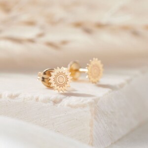May include: A pair of gold-toned stud earrings with a sun design. The earrings are small and delicate, and they would make a great gift for someone who loves the sun.