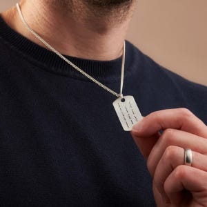 May include: A silver chain necklace with a rectangular silver tag pendant. The tag has an inscription on it.
