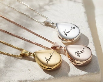 May include: Close-up of three teardrop-shaped lockets on delicate chains. The lockets are in silver, rose gold, and gold tones, each engraved with a name: "Family", "Amelia", and "Rose". The necklaces rest on a textured white surface.