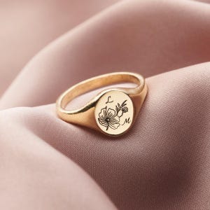 Può includere: Anello a sigillo in oro con un design floreale e le iniziali "L" e "M" incise sulla superficie.