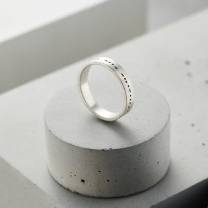 Puede incluir: Un anillo de banda de plata con un diseño simple de pequeños guiones alrededor de la banda.