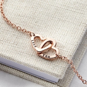 May include: Rose gold interlocking heart bracelet with the words "LOVE" and "YOU" engraved on the hearts.