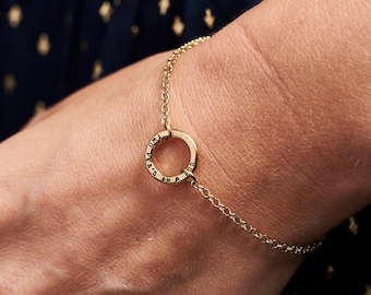 May include: A gold chain bracelet with a circular charm that reads "One Peak's in a Pod".