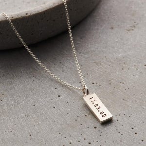 May include: A silver chain necklace with a rectangular pendant engraved with the date "17.03.09".