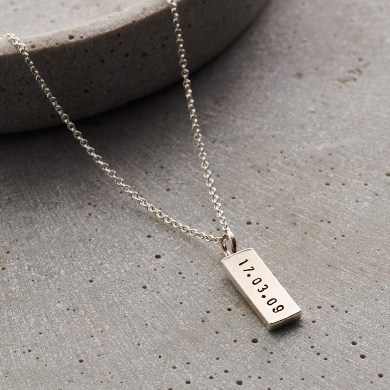 May include: A silver chain necklace with a rectangular pendant engraved with the date "17.03.09".