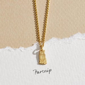 May include: A gold-colored necklace with a pendant shaped like a sitting cat. The cat pendant has detailed etched stripes. The necklace chain is also gold-colored. The word "Parsnip" is written in cursive below the necklace.