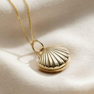 May include: A gold seashell locket necklace. The locket is shaped like a seashell and has a detailed design. The necklace is made of a delicate gold chain.