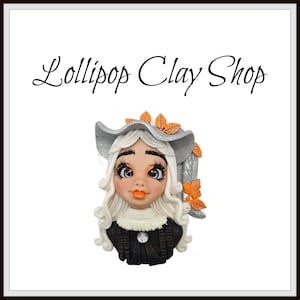 May include: A decorative clay figurine of a woman with long, curly white hair, wearing a silver hat adorned with orange leaves. The figurine has large eyes, orange lips, and a black and white outfit. The text "Lollipop Clay Shop" is above the figurine.