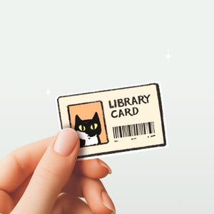 Puede incluir: Una pegatina rectangular de tarjeta de biblioteca con un gato negro de dibujos animados con ojos amarillos. La tarjeta tiene las palabras "LIBRARY CARD" impresas en negro, junto con un código de barras. El fondo es de color beige claro.