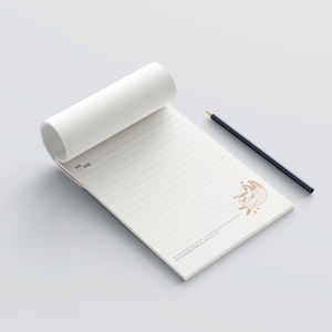 Peut inclure: Bloc-notes blanc cassé avec pages lignées et illustration de chat. Un crayon noir est posé à côté. Le bloc-notes est partiellement enroulé. Le crayon est noir.