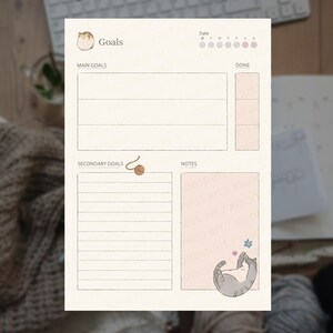 Puede incluir: Una hoja de planificación de objetivos de color crema con una ilustración de gato, un icono de ovillo de lana y secciones etiquetadas como Goals, Main Goals, Done, Secondary Goals y Notes. Incluye un rastreador de fechas semanal y un gato durmiendo.
