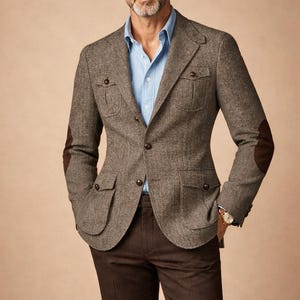 May include: A brown tweed blazer with elbow patches, paired with brown trousers and a light blue shirt. The blazer has multiple pockets and is buttoned. The image includes the text "MENFINITY SUITS".