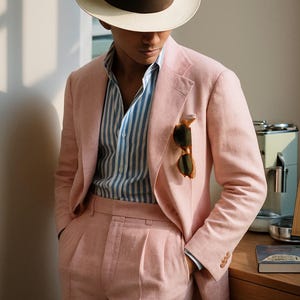 May include: A light pink suit with a matching jacket and pants. The jacket has a pocket square and sunglasses tucked in the pocket. A striped blue and white shirt is worn underneath. A cream-colored fedora hat with a brown band completes the look. The logo "MENFINITY SUITS" is visible.