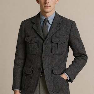 Könnte beinhalten: Ein anthrazitfarbener Blazer mit Fischgrätenmuster, vier aufgesetzten Vordertaschen mit geknöpften Klappen, steigendem Revers und einer Drei-Knopf-Vorderseite. Der Blazer wird über einem hellblauen Hemd mit Kragen und einer dunkelgrauen Krawatte getragen.
