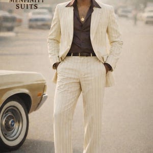 May include: A cream-colored pinstripe suit with a brown shirt and a gold pendant. The suit is worn with brown shoes and a black belt. The image includes the text "MENFINITY SUITS".