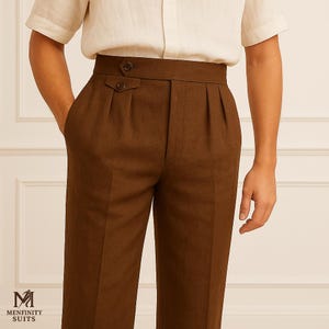 May include: Brown pleated trousers with a high waist and button details. The trousers are paired with a light-colored short-sleeved shirt. The image shows a close-up of the waist and upper legs. The brand logo "MENFINITY SUITS" is visible in the bottom left corner.