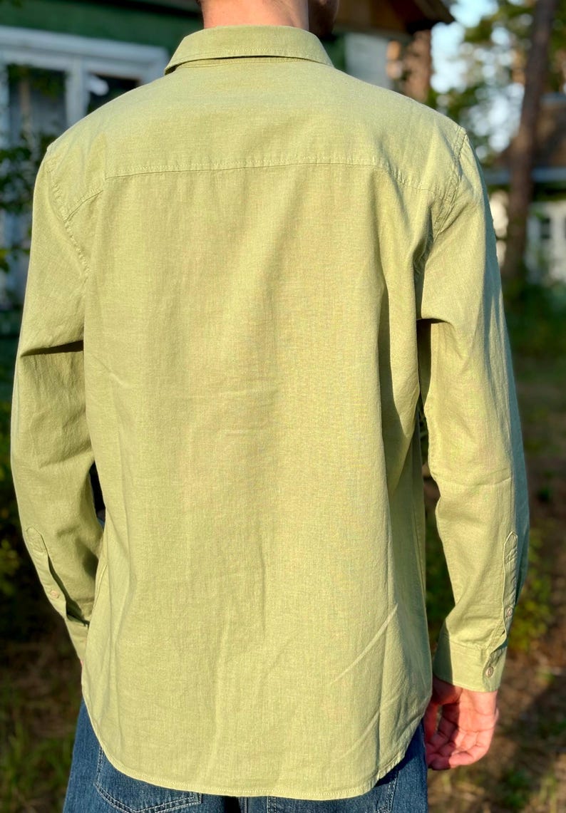Puede incluir: Una camisa de manga larga con botones en un color verde lima claro. La camisa presenta un cuello est&aacute;ndar, un canes&uacute; en la espalda y pu&ntilde;os abotonados en las mangas. La tela tiene una textura visible y la camisa se lleva sobre unos vaqueros azules.