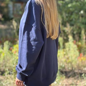 May include: A navy blue long-sleeved sweatshirt with a relaxed fit, featuring ribbed cuffs and a ribbed hemline. The garment is worn over light blue denim shorts, showcasing a simple and functional design with a solid dark blue colour throughout.