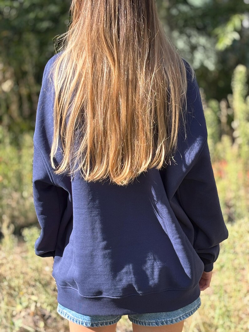 May include: A navy blue long-sleeved sweatshirt with a crew neckline and ribbed cuffs and hem, paired with light blue denim shorts. The sweatshirt features a loose, relaxed fit and is worn over the shorts, covering the upper portion of the legs.