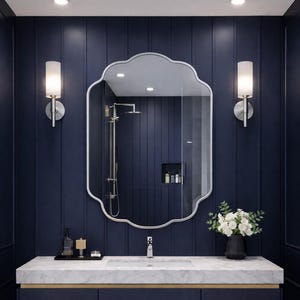 Op de afbeelding: Een moderne badkamer met marineblauwe lambrisering, een marmeren aanrechtblad en een marineblauwe wastafel. Boven de wastafel hangt een grote, sierlijke spiegel, en twee wandkandelaars flankeren de spiegel. Een vaas met witte bloemen staat op het aanrecht.