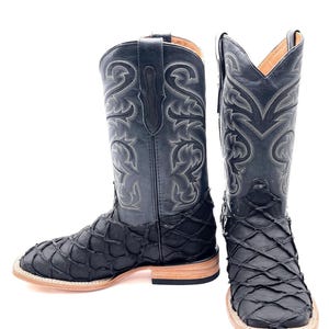 Könnte beinhalten: Schwarze Cowboy-Stiefel mit quadratischer Spitze und dekorativen Nähten. Der untere Teil des Stiefels hat ein strukturiertes, schuppenartiges Muster. Die Stiefel haben eine hellfarbige Sohle und einen Absatz.