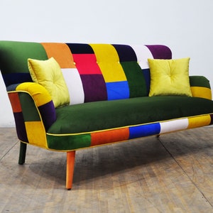 Può includere: Un divano patchwork colorato con una seduta in velluto verde e cuscini gialli. Il divano ha gambe in legno con accenti arancioni e neri.