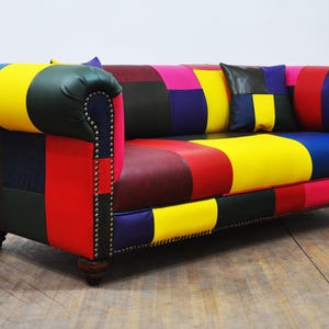 Puede incluir: Un sofá de patchwork colorido con una variedad de colores que incluyen rojo, amarillo, azul, verde y morado. El sofá tiene un respaldo y brazos capitoneados y está tapizado en una variedad de telas.