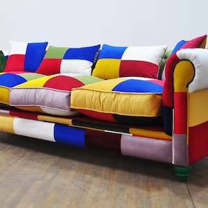 Può includere: Un divano patchwork colorato con una varietà di colori tra cui rosso, giallo, blu, verde e bianco. Il divano ha uno schienale trapuntato e braccioli arrotolati.