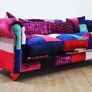 Puede incluir: Un sofá de patchwork colorido con una variedad de telas y patrones, incluyendo rosa, rojo, azul y verde. El sofá tiene un respaldo capitoné y un diseño con botones.