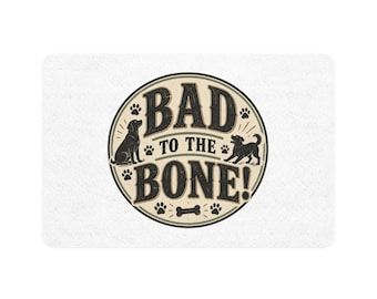 May include: A rectangular white doormat featuring a central circular graphic with the text BAD TO THE BONE! in black lettering. The design includes two black dog silhouettes, several paw prints, and a small bone icon on a beige background.