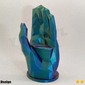 Puede incluir: Una escultura geométrica de una mano en tonos azules y verdes, con un diseño facetado. La escultura está sobre una base redonda y presenta el texto "@RyGuy Design".