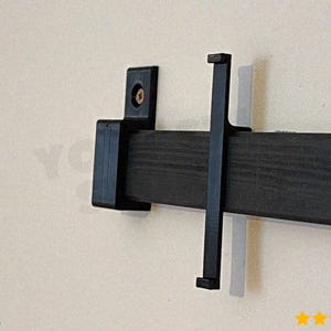 May include: Black wooden barn door hardware set, including a track and mounting brackets. The hardware is designed for a sliding door system. The set is mounted on a light beige wall. The brand name "wariat" is visible in the lower left corner.