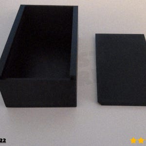 Puede incluir: Una caja rectangular negra con una tapa a juego. La caja est&aacute; abierta, revelando su interior. La tapa se coloca a un lado. La caja y la tapa est&aacute;n hechas de un material mate. La caja es probablemente para almacenamiento o exhibici&oacute;n.
