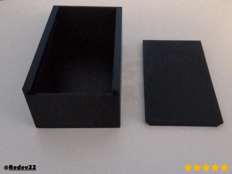 Puede incluir: Una caja rectangular negra con una tapa a juego. La caja est&aacute; abierta, revelando su interior. La tapa se coloca a un lado. La caja y la tapa est&aacute;n hechas de un material mate. La caja es probablemente para almacenamiento o exhibici&oacute;n.