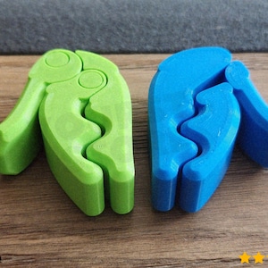 May include: Two plastic, claw-shaped tools, one green and one blue, are displayed on a wooden surface. The tools have a lever-like design with a curved gripping area. The green tool is on the left, and the blue tool is on the right.