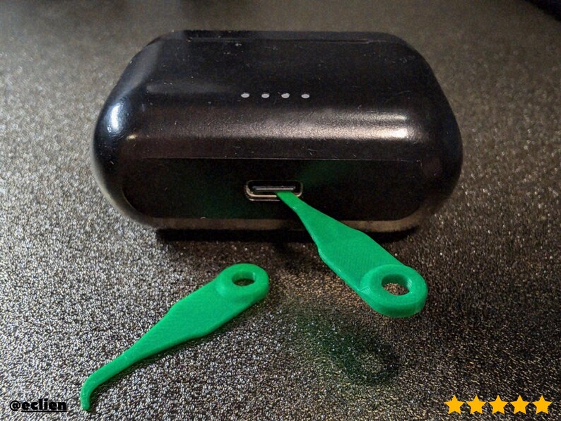 A close-up photograph of the 3D-printed electronic cleaning tool for a smartphone charging port, specifically designed for dust and lint removal. The image highlights the device's fine, precision-tip structure, crucial for deep port cleaning and maintenance of Lightning and USB-C connectors. This essential tech accessory is shown on a clean surface, emphasizing its small size and efficient design.