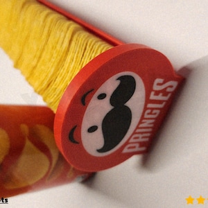 Może przedstawiać: Czerwono-biała puszka chipsów Pringles z żółtym stosikiem chipsów. Logo Pringles jest widoczne na czerwonej pokrywce. Chipsy są ułożone wewnątrz puszki. Obraz jest dobrze oświetlony i kolory są żywe.