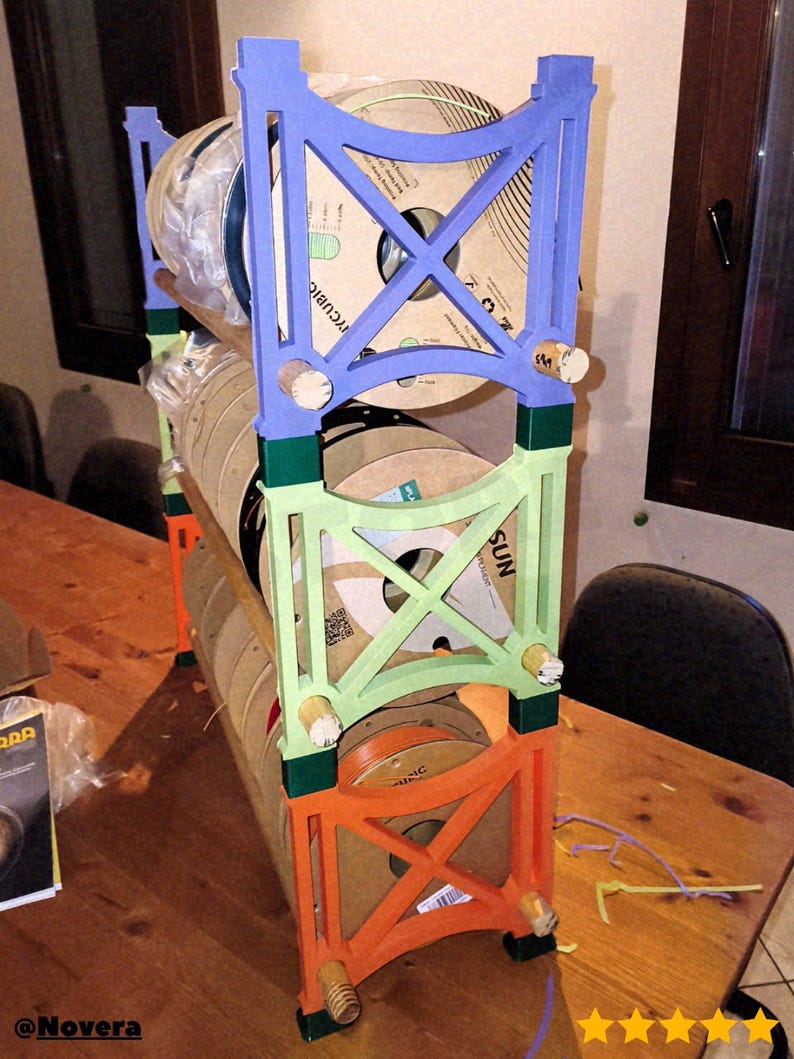 May include: A multi-colored, three-tiered spool rack. The rack is constructed from wood and painted in blue, green, and orange. Each level holds several spools of filament. The rack is designed to organize and display 3D printing filament.