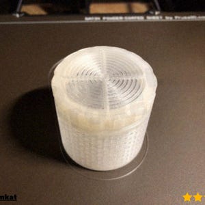 Könnte beinhalten: Ein zylindrisches, durchscheinendes 3D-gedrucktes Objekt in Weiß mit einem Spiralmuster auf der Oberseite. Es steht auf einer dunkelbraunen Oberfläche. Der Text "@Fathomkat" ist sichtbar.