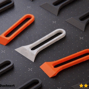 May include: An assortment of scraper tools in various colors, including orange, white, and gray. Each scraper has a handle with a rectangular opening and a blade. The tools are arranged on a dark surface.