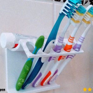 May include: A white plastic toothbrush holder with multiple toothbrushes and a tube of toothpaste. The toothbrushes are various colors, including blue, green, orange, and purple. The toothpaste tube is white with red accents.